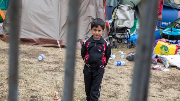Ein Junge steht vor einem Zaun in einem Lager mit Zelten und Müll.