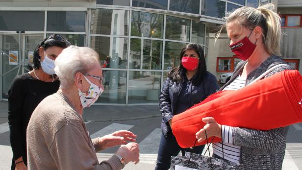 Die jungen Leute bringen der alten Frau den Stoff, aus dem sie Nase-Mund-Schutzmasken nähen wird