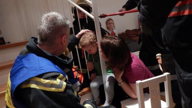 Ein Feuerwehrmann tröstet ein Kind auf einer Treppe, während eine Frau daneben kniet.