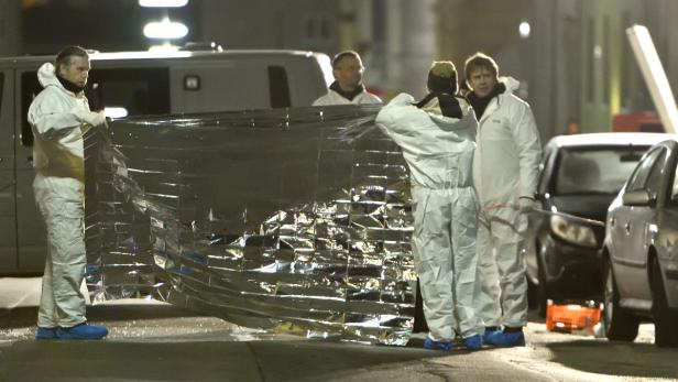 Mehrere Personen in Schutzanzügen hantieren mit einer silbernen Plane auf einer Straße.