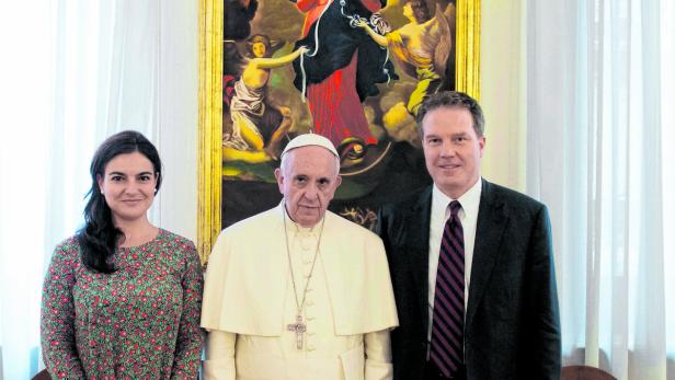 Papst Franziskus posiert mit zwei Personen vor einem Gemälde.