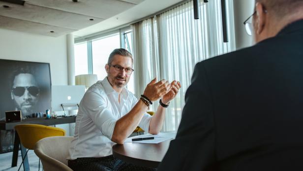 Ein Mann mit Brille gestikuliert während eines Gesprächs an einem Tisch.