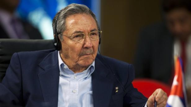 Raúl Castro trägt ein Headset und sitzt an einem Tisch mit der kubanischen Flagge.