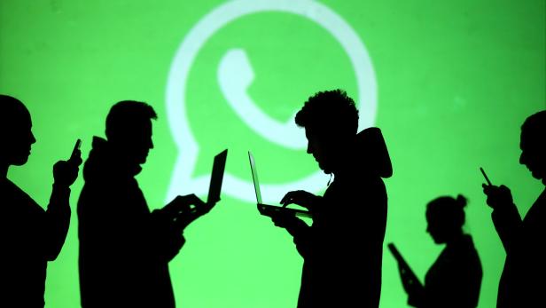 Silhouetten von Personen mit Laptops und Smartphones vor einem WhatsApp-Logo.