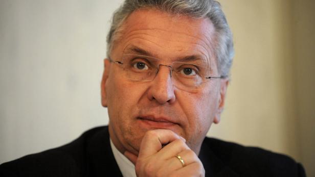 Ein Mann mit Brille und Anzug hält seine Hand ans Kinn.