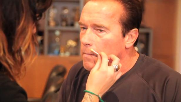 Arnold Schwarzenegger wird von einer Maskenbildnerin geschminkt.