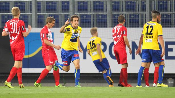 Ein Fußballspieler in Gelb jubelt, während andere Spieler in Rot und Gelb im Hintergrund stehen.