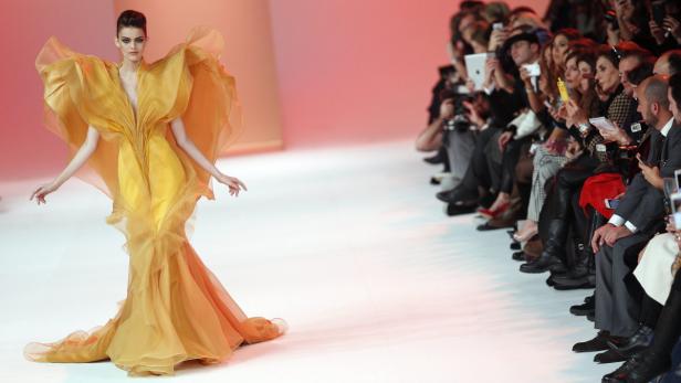 Ein Model präsentiert ein gelbes Kleid mit voluminösen Stoffbahnen auf einem Laufsteg.