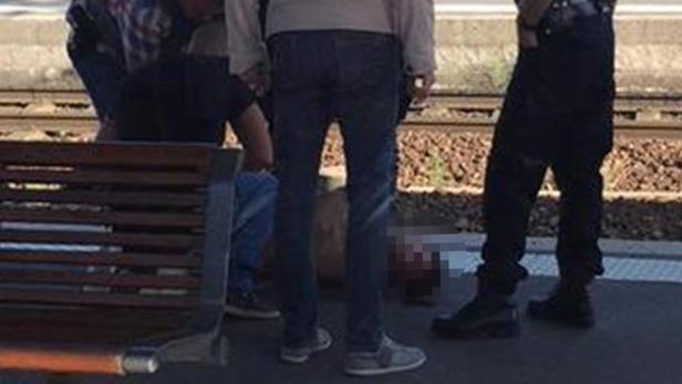 Mehrere Personen stehen um eine am Boden liegende Person auf einem Bahnsteig.