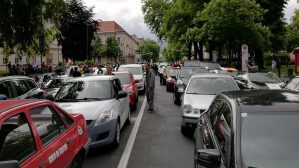 Eine Menschenmenge steht zwischen parkenden Autos auf einer Straße.