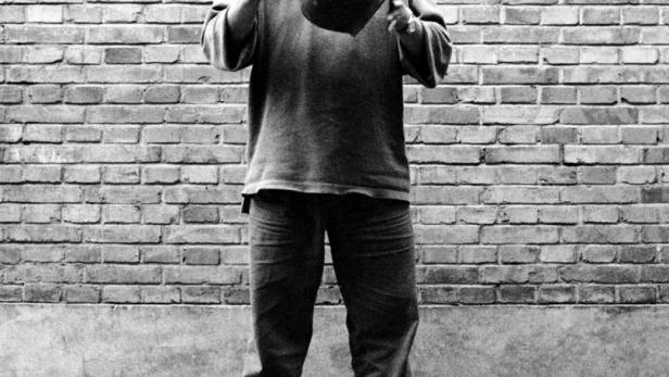 Ein Mann hält eine große Vase vor einer Ziegelwand.