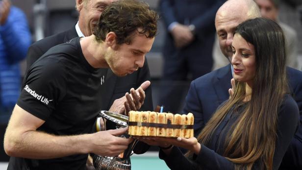 Andy Murray pustet eine Kerze auf einer Torte aus, die von einer Frau gehalten wird.