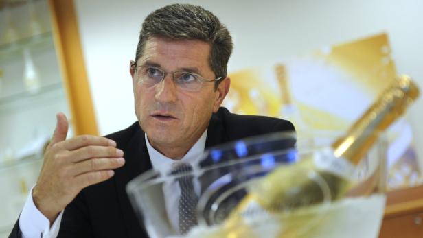 Ein Mann mit Brille gestikuliert neben einer Champagnerflasche im Eis.