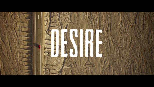 Ein rotes Auto fährt auf einer Straße durch eine Wüstenlandschaft. Im Vordergrund steht das Wort „Desire“.
