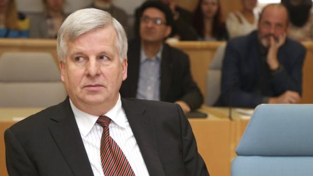 Ein Mann mit grauem Haar und Anzug sitzt in einem Publikum.