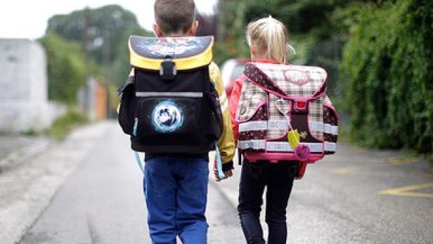 Ein Junge und ein Mädchen mit Schulranzen gehen eine Straße entlang.