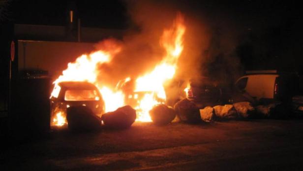 Mehrere Autos stehen in Flammen, mit großen Felsbrocken davor.