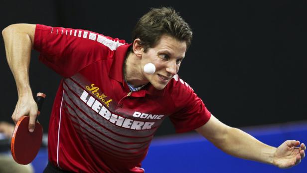 Ein Tischtennisspieler in rotem Trikot schlägt einen Ball.