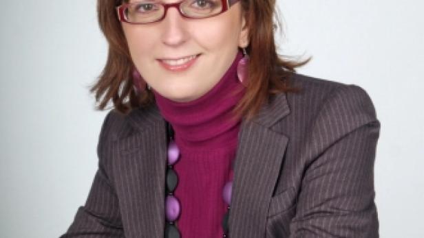 Eine Frau mit Brille, lila Rollkragenpullover und Blazer lächelt in die Kamera.