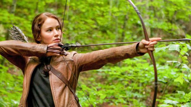 Jennifer Lawrence zielt mit Pfeil und Bogen in einem Wald.