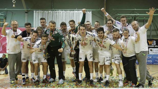 Eine Handballmannschaft feiert einen Sieg mit einem Pokal und Konfetti.