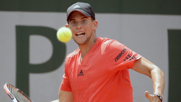 Dominic Thiem bei einem Tennisspiel im roten Trikot mit dem Ball vor dem Gesicht.