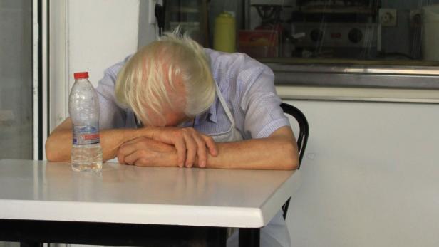 Ein Mann mit blonden Haaren schläft mit dem Kopf auf dem Tisch neben einer Wasserflasche.