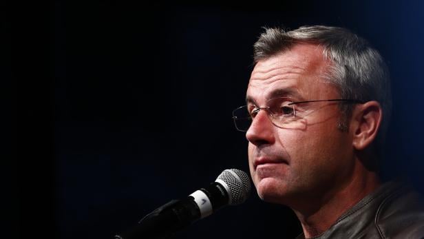 Ein Mann mit Brille und grauen Haaren spricht in ein Mikrofon, dunkler Hintergrund.