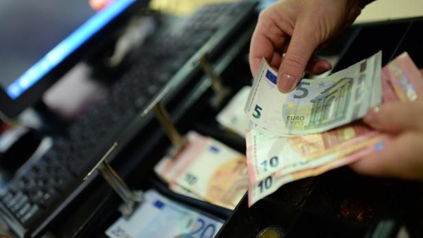Eine Hand zählt Euroscheine über einer geöffneten Kasse.