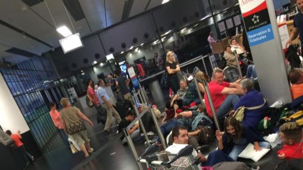 Viele Menschen warten mit ihrem Gepäck auf dem Boden eines Flughafens.