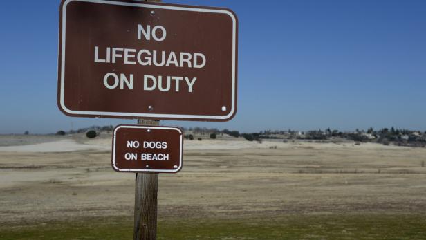 Ein Schild warnt: „Kein Rettungsschwimmer im Dienst“ und „Keine Hunde am Strand“.