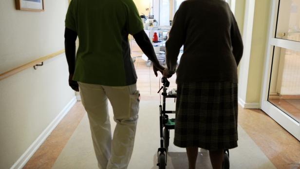Pflegekraft hilft alter Frau mit Rollator im Pflegeheim.