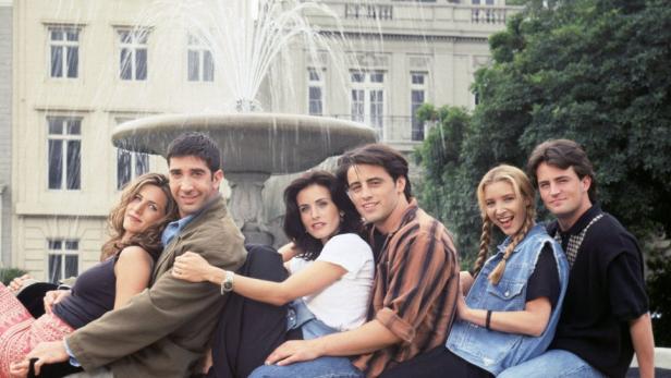 Die sechs Hauptdarsteller der Fernsehserie „Friends“ sitzen vor einem Brunnen.
