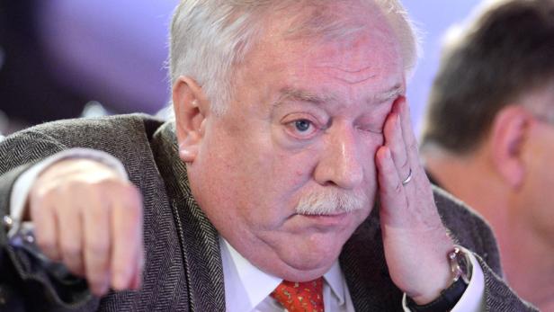 Ein Mann mit Schnurrbart hält seine Hand vor sein Gesicht.