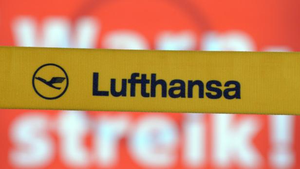 Ein gelbes Band mit dem Lufthansa-Logo vor einem verschwommenen Streik-Schild.