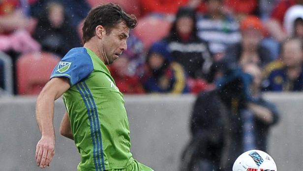 Ein Fußballspieler in Grün und Blau schießt einen Ball.