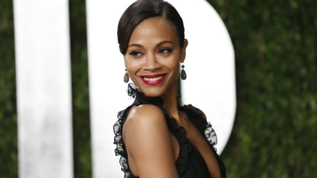 Zoe Saldana lächelt in einem schwarzen Kleid mit Rüschen und roten Lippenstift.