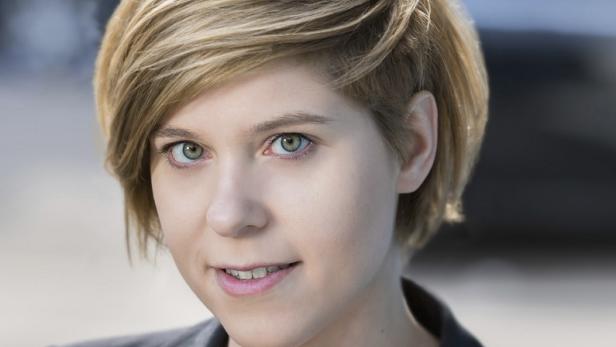 Porträt einer jungen Frau mit blonden, kurzen Haaren und hellen Augen.