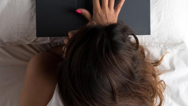 Eine Frau liegt im Bett und tippt auf einem Laptop.