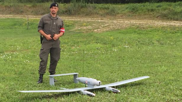 Ein Soldat steht neben einer Aufklärungsdrohne auf einer Wiese.