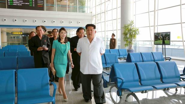 Kim Jong-un und seine Frau gehen durch einen hellen Flughafen.