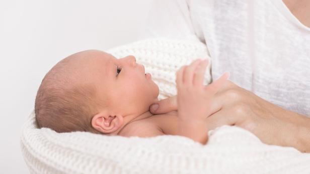 Ein Neugeborenes liegt in einer weißen Decke und wird von einer Person im Arm gehalten.