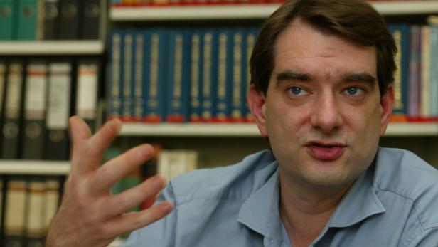 Ein Mann gestikuliert vor einem Bücherregal.