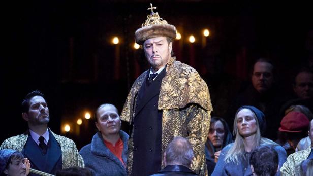 Ein Mann in historischer Kleidung und Krone steht auf einer Bühne vor Publikum.