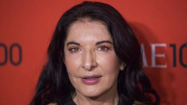 Ein Porträt der Künstlerin Marina Abramović vor einem roten Hintergrund.
