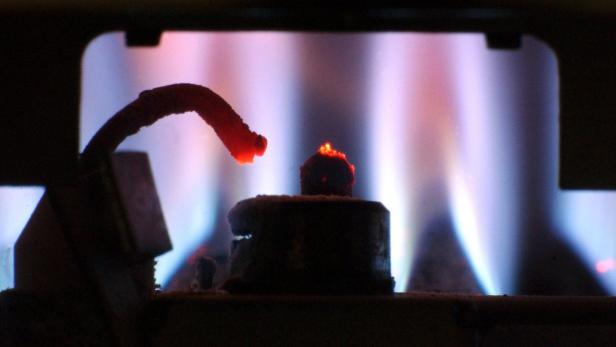 Die Zündflamme eines Gasbrenners leuchtet rot vor blauem Hintergrund.