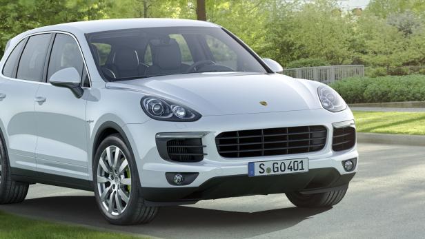 Ein weißer Porsche Cayenne parkt vor einer grünen Hecke.