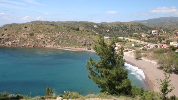 Blick auf eine malerische Bucht mit Sandstrand und kleinen Häusern im Hintergrund.