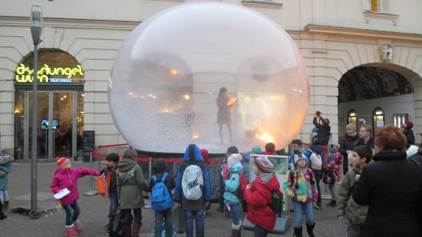 Eine Gruppe Kinder steht vor einer großen Schneekugel vor dem Theaterhaus Dschungel Wien.