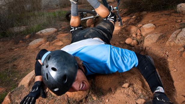 Ein Mountainbiker ist gestürzt und liegt auf einem steinigen Hügel.